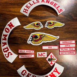 Puede incluir: Una colección de parches bordados con fondo blanco, texto rojo y motivos de calaveras aladas amarillas. El texto incluye HELLS ANGELS, NOMADS, GERMANY, AFFA, FILTHY FEW, SGTATARMS, PRESIDENT, MC, 666 y un parche en forma de diamante 1% con calavera.