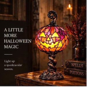 May include: A stained glass pumpkin lamp with a jack-o'-lantern face in shades of orange and purple, featuring a twisted metal base and a pull chain. Text on the left reads: A LITTLE MORE HALLOWEEN MAGIC. Light up a spooktacular season.