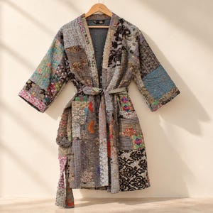 May include: A long-sleeved robe featuring a patchwork design with various grey, brown, and multicoloured fabric panels. The garment includes a matching tie belt at the waist, an open front, and a quilted texture throughout the entire piece.