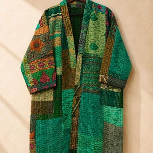 Op de afbeelding: Een jas met lange mouwen in kimonostijl met een patchworkontwerp in verschillende tinten groen, waaronder smaragd, olijf en limoen. Het kledingstuk is opgebouwd uit meerdere stoffen panelen met zichtbare witte doorstikdetails.