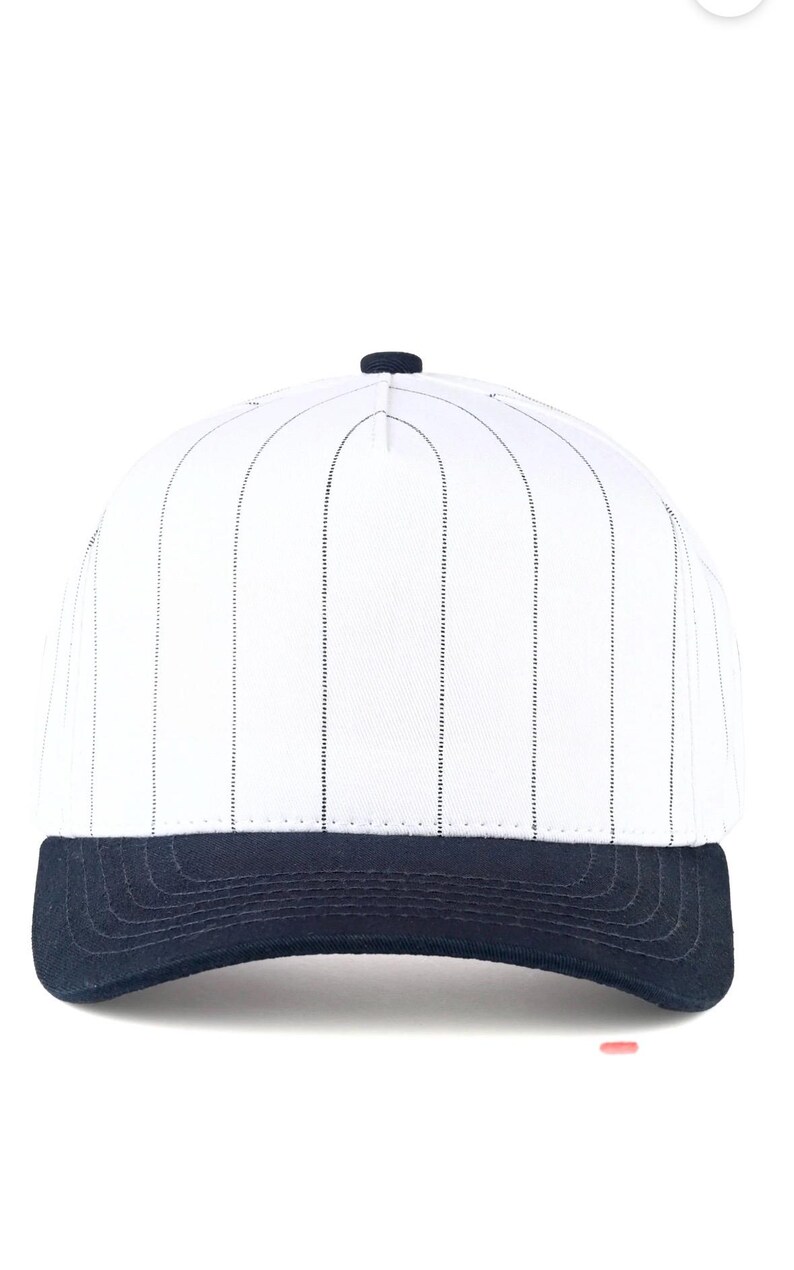 May include: White baseball cap with vertical black pinstripes and a navy blue brim. The cap has a rounded crown and a button on top. This classic style is suitable for sports or casual wear.