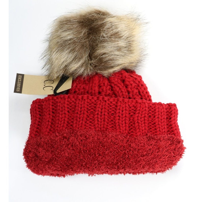 May include: Red knit beanie with a fluffy brown and beige pom pom. The beanie has a fleece lining and a tag that reads "C.C. Exclusives".