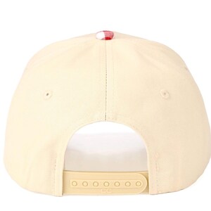 Puede incluir: Una gorra de b&eacute;isbol de color crema con un bot&oacute;n de patr&oacute;n de cuadros vichy rojo y blanco en la parte superior. La parte trasera de la gorra incluye un cierre ajustable de pl&aacute;stico con las letras CC grabadas en la leng&uuml;eta central.