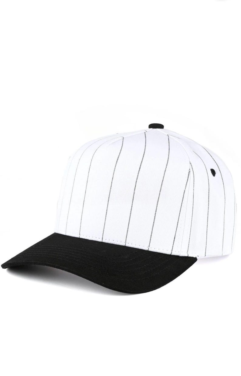 May include: White baseball cap with black pinstripes and a black brim. The cap has a rounded crown and a small black button on top. A classic style for sports or casual wear.