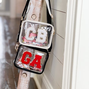 Puede incluir: Dos bolsos de bandolera de pl&aacute;stico transparente con correas negras. El bolso de arriba tiene las letras blancas "CB". El bolso de abajo tiene las letras rojas "GA".