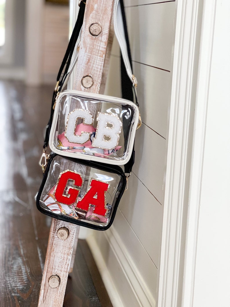 Puede incluir: Dos bolsos de bandolera de pl&aacute;stico transparente con correas negras. El bolso de arriba tiene las letras blancas "CB". El bolso de abajo tiene las letras rojas "GA".