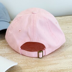 May include: A pink baseball cap with a brown adjustable strap in the back.