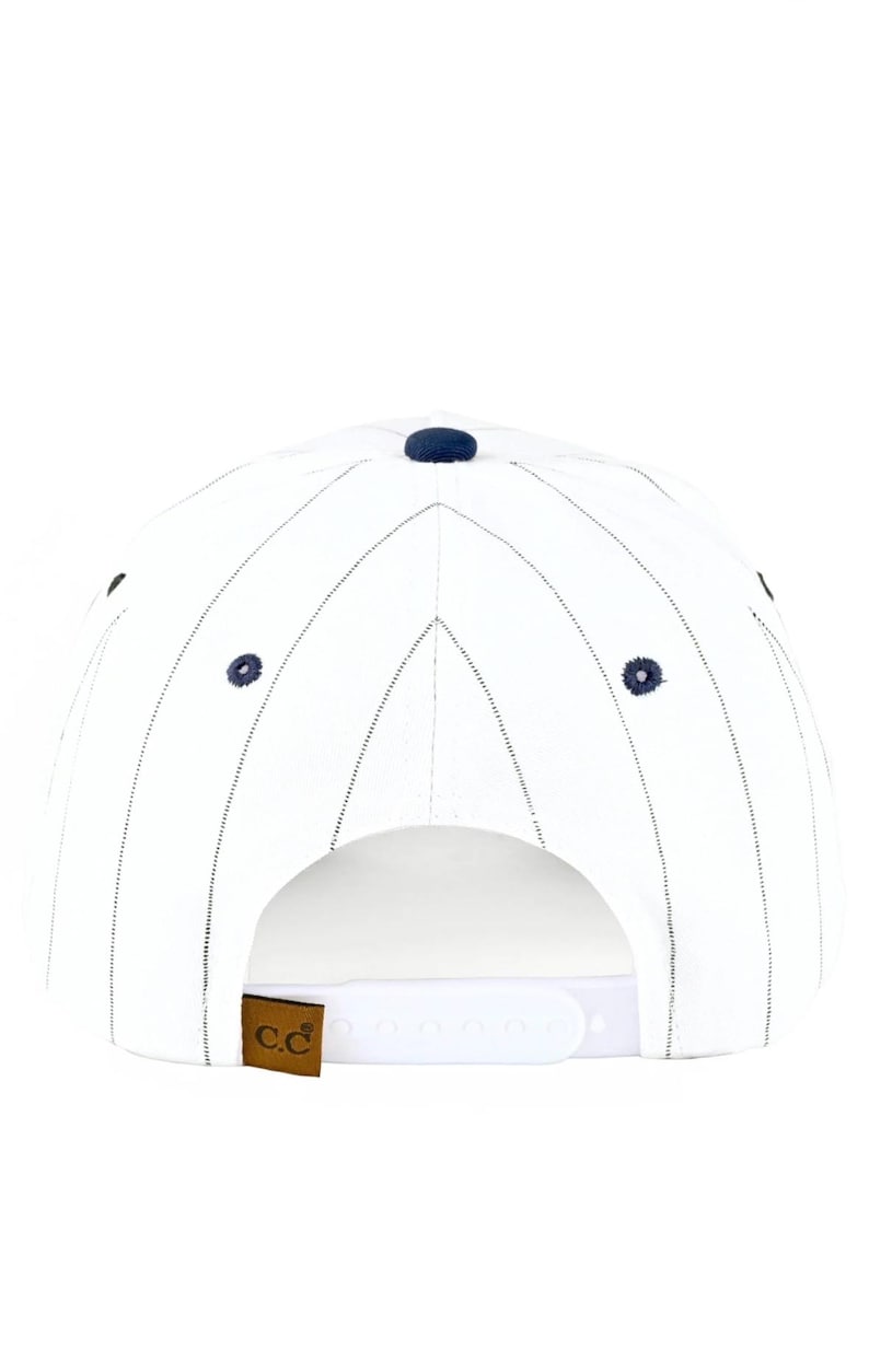 May include: White baseball cap with navy blue pinstripes and a navy blue button on top. The cap has a curved brim and a white adjustable snap closure. A brown leather tag with the letters "c.c" is attached to the back.