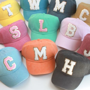 May include: Assortment of 10 baseball caps in various colors with a large letter on the front of each cap. The letters are white with gold glitter trim. The caps are made of a soft, cotton fabric.