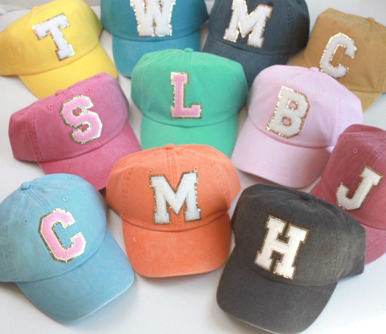 May include: Assortment of 10 baseball caps in various colors with a large letter on the front of each cap. The letters are white with gold glitter trim. The caps are made of a soft, cotton fabric.