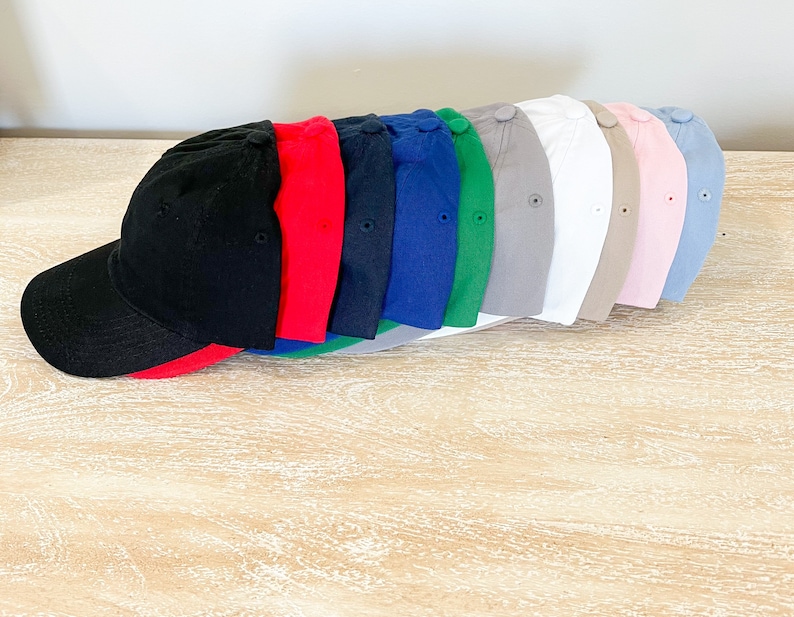 May include: A row of ten blank baseball caps in various colors, including black, red, blue, green, gray, white, beige, pink, and light blue. The caps are arranged in a line, with the black cap at the front and the light blue cap at the back.
