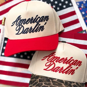 Puede incluir: Dos gorras de b&eacute;isbol con coronas de color crema y el texto bordado American Darlin'. Una gorra tiene una visera roja s&oacute;lida, mientras que la otra tiene un estampado de leopardo marr&oacute;n y negro. Ambas tienen un dise&ntilde;o de cinco paneles.