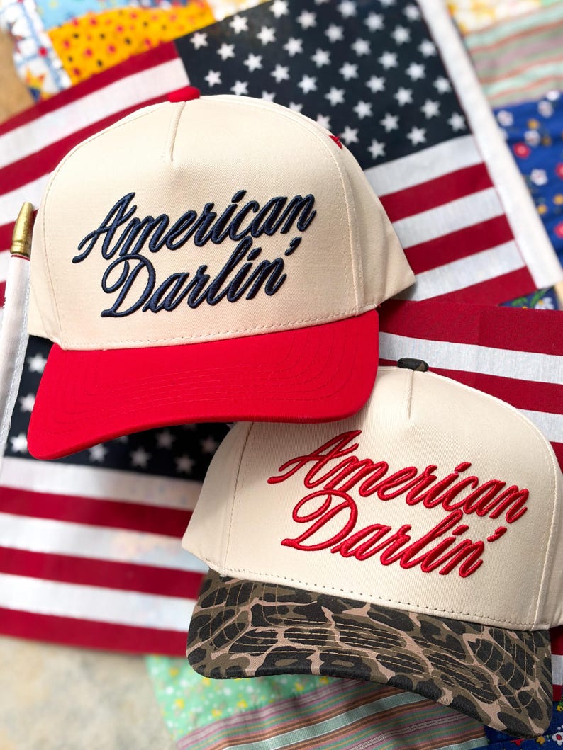 Puede incluir: Dos gorras de b&eacute;isbol con coronas de color crema y el texto bordado American Darlin'. Una gorra tiene una visera roja s&oacute;lida, mientras que la otra tiene un estampado de leopardo marr&oacute;n y negro. Ambas tienen un dise&ntilde;o de cinco paneles.