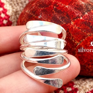 Puede incluir: Un anillo de plata con un diseño en espiral de varias capas con bandas planas y pulidas que se envuelven alrededor del dedo. El texto silvoraa925 está impreso en el lado derecho del anillo, junto a un pequeño icono de hoja.