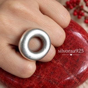 May include: A circular silver ring with a smooth, matte finish and a thick, rounded band. The ring features a simple, continuous loop design. The text silvoraa925 is visible on the right side of the image, accompanied by a small heart icon.
