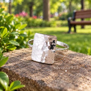 May include: A silver ring featuring a large, rectangular, hammered metal plate as the centrepiece. The surface of the plate has a textured, dimpled finish that reflects light. The band is smooth and circular. The text "silvoraa925" is visible.