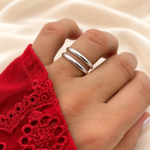 May include: A double band ring featuring two smooth, polished silver-toned metal bands that sit parallel on the finger. The design consists of two separate, rounded, solid metal loops that create a stacked appearance on the finger.