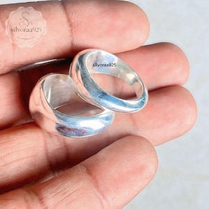 May include: Two polished silver rings with a smooth, rounded band design. The rings feature a high-shine metallic finish and a simple, solid construction. The text silvoraa925 is visible on the surface of the smaller ring and in the top corner.