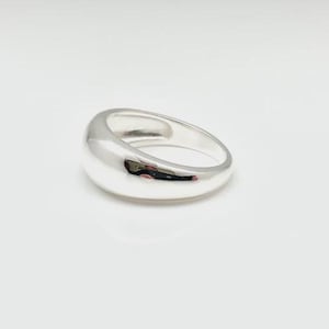 May include: A polished silver-tone dome ring with a smooth, rounded surface and a thick, tapered band. The metal has a high-shine, reflective finish that catches the light, creating a clean, solid, and continuous circular shape.