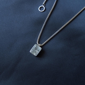 May include: A silver-toned box chain necklace featuring a rectangular pendant with a clear, faceted stone containing dark, branch-like inclusions. The necklace includes a small circular clasp ring at the top, showcasing a metallic finish throughout.