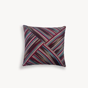 May include: A square throw pillow featuring a geometric pattern of diagonal stripes in shades of deep burgundy, dark brown, white, and bright turquoise. The fabric design is arranged in four triangular sections that meet at the center.