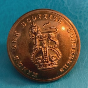 May include: A round, metallic gold-coloured button featuring an embossed design of a lion standing atop a crown. The text "KING'S OWN SCOTTISH BORDERERS" is engraved in a circular pattern around the central emblem on the face of the button.