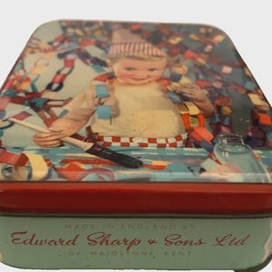 May include: A rectangular metal tin with a red lid and light blue sides. The lid features a vintage illustration of a child wearing a striped hat, surrounded by colourful paper chains and holding a paintbrush. Text reads: MADE IN ENGLAND BY Edward Sharp & Sons Ltd OF MAIDSTONE KENT.