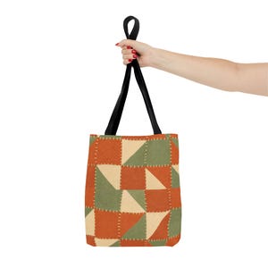 May include: A tote bag featuring a patchwork design of triangles in burnt orange, sage green, and cream colours. The pattern includes white dashed lines that mimic hand-stitched details between the fabric sections. It has two black fabric handles.