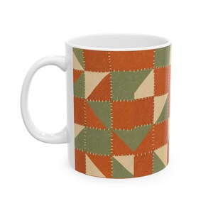 May include: A white ceramic mug featuring a repeating patchwork quilt pattern. The design consists of squares and triangles in shades of burnt orange, sage green, and cream, with white dashed lines simulating hand-stitched seams throughout.