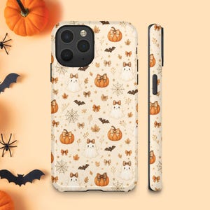 Puede incluir: Una funda para teléfono con un patrón repetitivo de calabazas naranjas, fantasmas blancos, murciélagos marrones, telarañas y pequeños lazos sobre un fondo crema claro. El diseño se muestra tanto en la parte trasera como en el lateral.