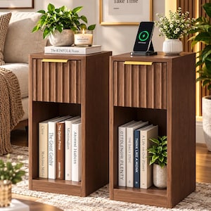 May include: Two matching dark wood nightstands, each featuring a single drawer with a vertical fluted front and a slim gold handle. Below the drawer is an open storage shelf. The nightstands are styled with books, small potted plants, and a wireless phone charger.