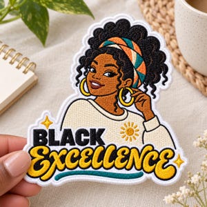 May include: An embroidered patch featuring a person with dark skin, curly hair, and a colorful headband, wearing large gold hoop earrings. The text "BLACK EXCELLENCE" is stitched in bold black and yellow letters, accented by a small sun and star icons.