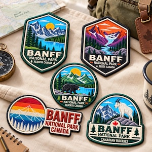 May include: Five embroidered patches featuring Banff National Park. Designs include mountain landscapes, a black bear, a mountain goat, and a sunset, all with the text Banff National Park Alberta Canada or Canadian Rockies stitched in various colors.