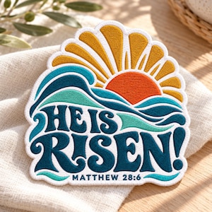 May include: An embroidered patch featuring a rising sun in yellow and orange above teal and blue waves. The text HE IS RISEN! is stitched in dark blue, with MATTHEW 28:6 in smaller dark blue letters at the bottom, all on a white background.