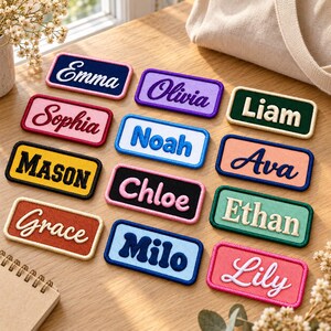 K&ouml;nnte beinhalten: Eine Sammlung rechteckiger, bestickter Namensaufn&auml;her in verschiedenen Farben wie Pink, Blau, Gelb, Gr&uuml;n und Lila. Jeder Aufn&auml;her zeigt einen individuellen Namen, der mit kontrastierendem Garn gestickt ist, darunter Emma, Olivia, Liam, Sophia, Noah, Ava, Mason, Chloe, Ethan, Grace, Milo und Lily.