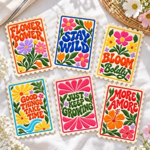May include: Six rectangular embroidered patches with scalloped edges, each featuring colorful floral designs and text: FLOWER POWER, STAY WILD, BLOOM BOLDLY, GOOD THINGS TAKE TIME, JUST KEEP GROWING, and MORE AMORE, all with green leaves.