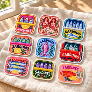May include: A collection of nine embroidered patches featuring sardine-themed designs. Each square patch displays colorful illustrations of fish, lemons, and mermaids, with the text SARDINES printed on several of the individual designs.