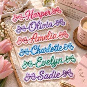 May include: Six embroidered name patches featuring the names Harper, Olivia, Amelia, Charlotte, Evelyn, and Sadie. Each patch is stitched in a distinct color with a decorative bow on both the left and right sides of the cursive lettering.