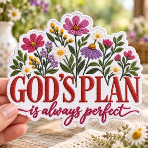 May include: A white embroidered patch featuring a floral arrangement of pink, purple, yellow, and white flowers with green leaves. The text reads GOD'S PLAN in bold red capital letters and is always perfect in red cursive script.