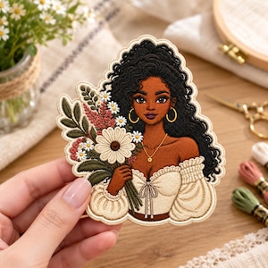 May include: An embroidered patch featuring a person with dark skin and long, wavy black hair, wearing a cream-colored off-the-shoulder top with puffed sleeves. The person holds a bouquet of white daisies, pink flowers, and green foliage.