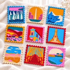 May include: Nine square embroidered patches with scalloped edges, each featuring a different colorful landscape or architectural scene, including waterfalls, city skylines, mountains, desert vistas, and a red bridge, arranged in a grid pattern.