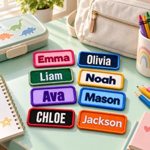 May include: A collection of eight rectangular embroidered name patches in various colors including pink, dark blue, green, cream, purple, light blue, black, and orange, each featuring a white or dark name stitched in a bold, sans-serif font.
