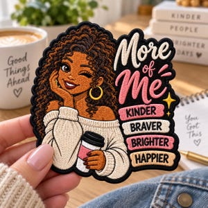 May include: An embroidered patch featuring a person with curly brown hair, gold hoop earrings, and a cream-colored sweater holding a coffee cup. The text reads: More of Me, Kinder, Braver, Brighter, Happier. The design has a black border.