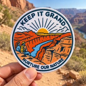 May include: A circular embroidered patch featuring a canyon landscape with a blue river, orange rock formations, and a yellow sun. Two figures sit on the edge. The text reads KEEP IT GRAND and NURTURE OUR NATURE in dark blue lettering.