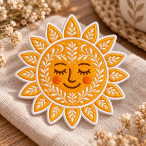 May include: A circular embroidered patch featuring a stylized sun with a smiling face, closed eyes, and orange cheeks. The sun has golden yellow rays decorated with white leaf patterns, and the central face is surrounded by a white floral border.