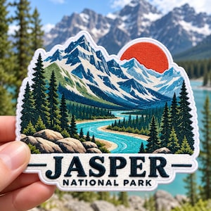 May include: An embroidered patch featuring a mountain landscape with snow-capped peaks, a bright orange sun, a winding turquoise river, and dark green pine trees. The bottom white border displays the text JASPER NATIONAL PARK in black.