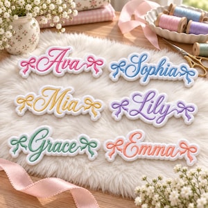 May include: Six embroidered name patches on a white faux fur surface. The names Ava, Sophia, Mia, Lily, Grace, and Emma are stitched in cursive script with matching colored bows on each side. The patches are white with colored thread borders.