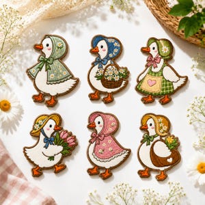 May include: Six embroidered patches featuring white ducks with orange beaks and feet. Each duck wears a different colored bonnet and outfit, including floral patterns, a basket of daisies, a pink tulip bouquet, and a green apron with a heart.