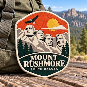 May include: An embroidered patch featuring the Mount Rushmore monument with four presidential faces, a flying bald eagle, and a yellow sun against an orange sky. The dark green base displays the text MOUNT RUSHMORE SOUTH DAKOTA.