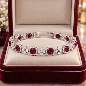 Puede incluir: Una pulsera de tono plateado que presenta una alternancia de piedras rojas de corte cuadrado y grupos de cuatro piedras blancas redondas. La pieza incluye un mecanismo de cierre metálico seguro y se exhibe en un joyero de terciopelo rojo.